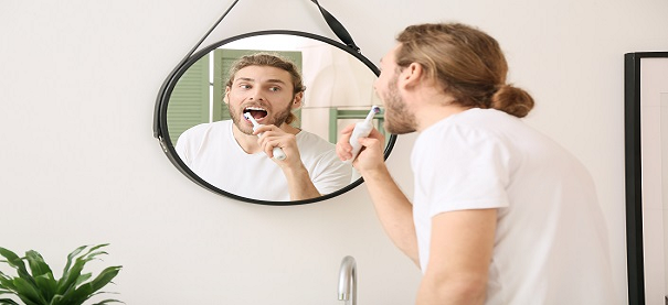Man looks in the mirror while brushing his teeth with an electric toothbrush.